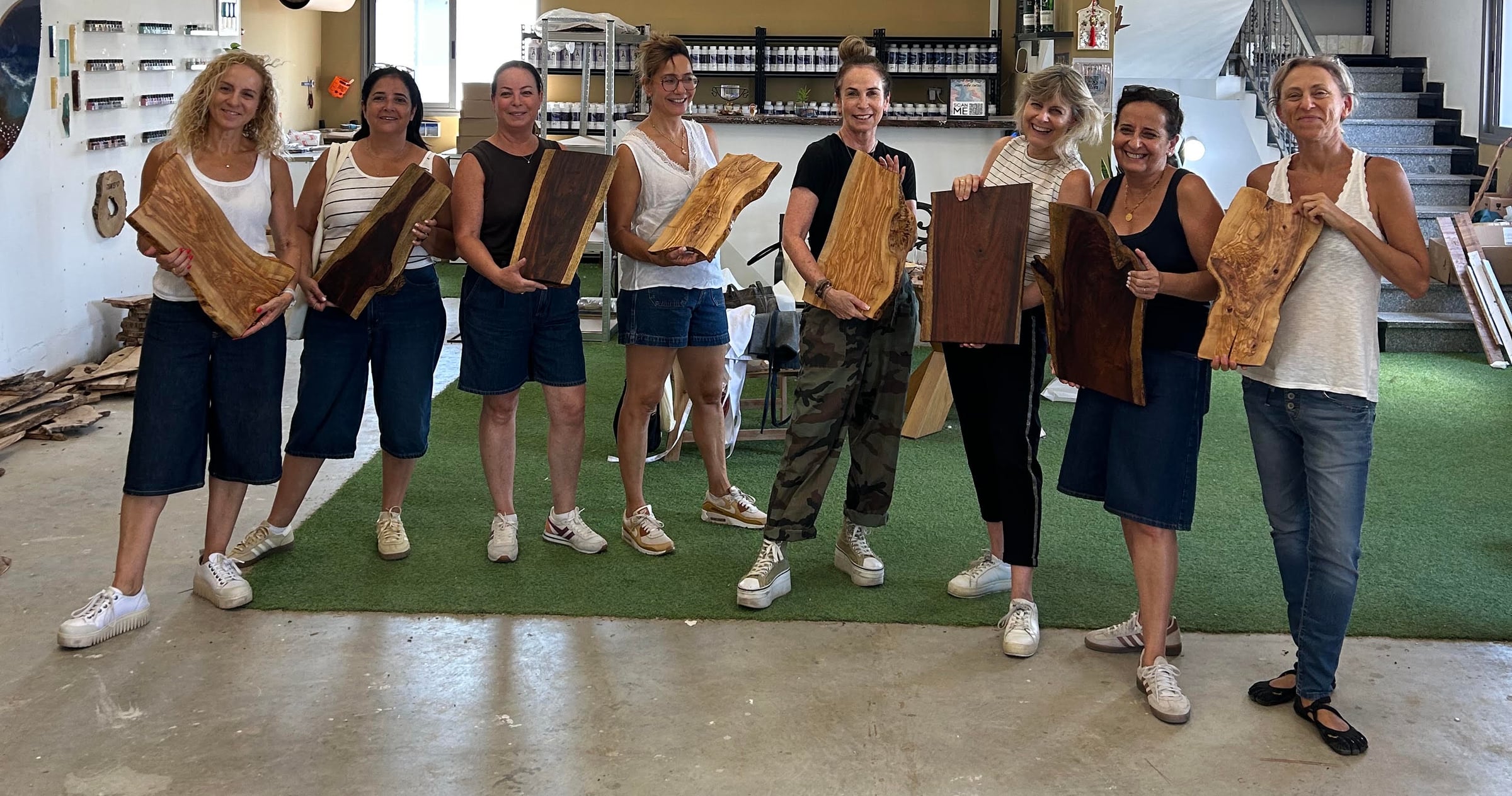 קבוצת משתתפות מציגות בגאווה קרשי חיתוך מעץ טבעי שהכינו בסדנת גיבוש