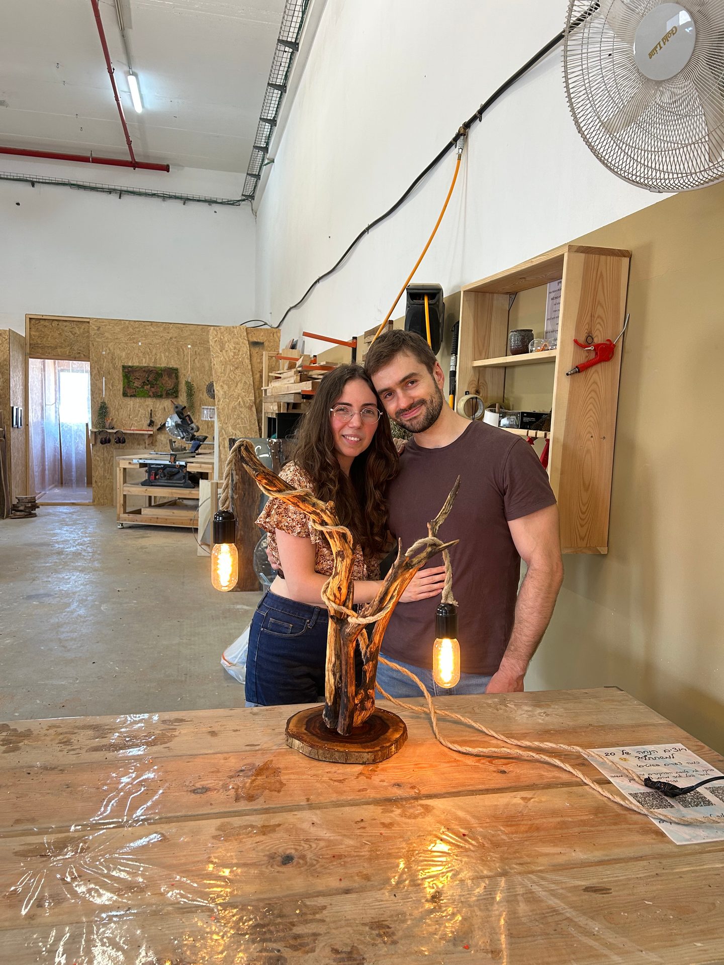 זוג מציג מנורת ענף מעץ טבעי מוגמרת שיצרו בסדנה